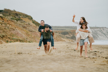 A group of people are playing a game of tag on a beach. Scene is lighthearted and fun, as the group of people are enjoying themselves and running around in the sand