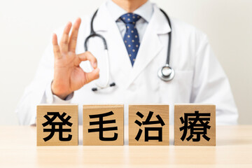 「発毛治療」と書かれたブロックとOKサインをする医師