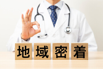 「地域密着」と書かれたブロックとOKサインをする医師
