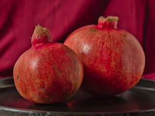 Still Life with Two Ripe Pomegranates on a Purple Red Background