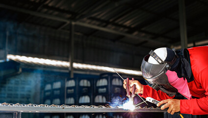 Welder wearing a red long-sleeved shirt and a protective mask is welding a steel grating, Industrial Welder With Torch