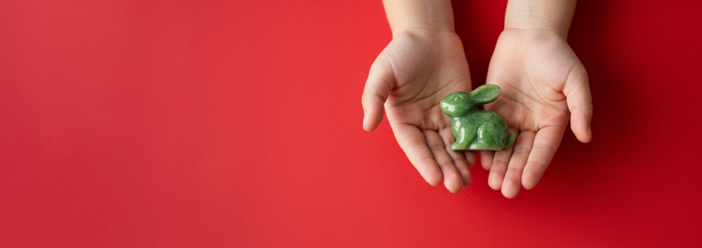 Jade rabbit statue held by child hands on red background, symbolizing Lunar New Year tradition