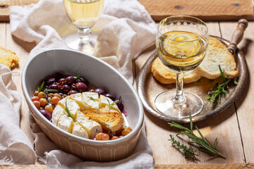 Baked Camembert cheese with grapes, thyme, and rosemary, served with white wine and a baguette.
