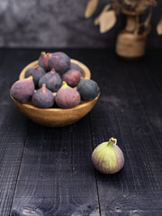 Dark rustic setup showing figs in wooden bowls, one fig in the foreground and vase decor creating depth and texture in the background