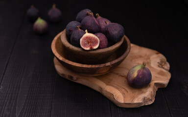 Half sliced fig in two stacked wooden bowls on serving plate with whole figs arranged in front and back, rustic dark still life
