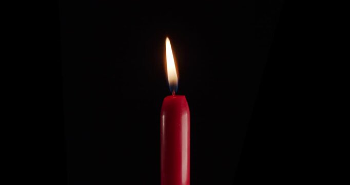 A single red candle burning. Isolated candle burning with dark background. Red paraffin candle with yellow shades burns on a black background. Background or illustration of remembrance or celebration.