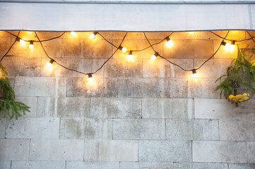 String lights glowing on a stone wall with pine branches create festive Christmas outdoor holiday decor