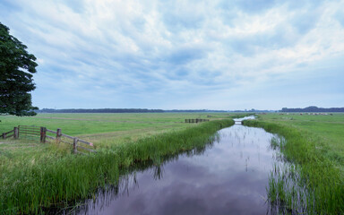 Calm water reflects the cloudy sky over fields