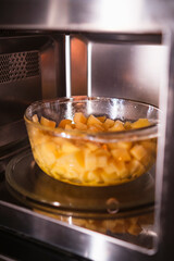 Putting a bowl with raw peeled potatoes in microwave. Cooking at home. Fresh homemade food.