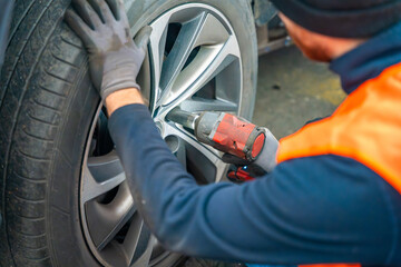 Mechanic using an impact wrench to remove lug nuts from a car wheel. Seasonal tire change and professional car service in preparation for winter.
