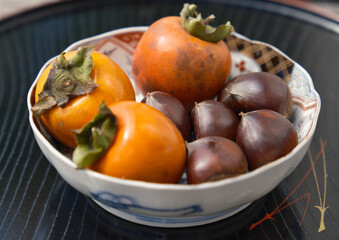 Japanese autumn delicacies: A still life of vibrant persimmons and chestnuts beautifully arranged on a traditional lacquerware tray and rustic wooden surface. Capturing the essence of seasonal food, J