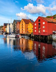 Obraz premium A stunning waterfront scene in Norway, featuring colorful buildings reflected in the still, blue water. The sky is bright with fluffy white clouds