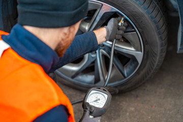 Obraz premium Worker checking tire pressure with gauge after seasonal wheel replacement. Final step of winter tire preparation in auto service in Czech Republic.