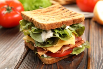 Tasty sandwich with bacon, cheese, vegetables and sauce on wooden table, closeup