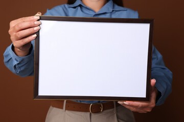 Naklejka premium Woman with blank diploma frame on brown background, closeup. Mockup for design