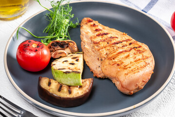 Grilled chicken breast served with colorful vegetables on a plate at a casual dining setting