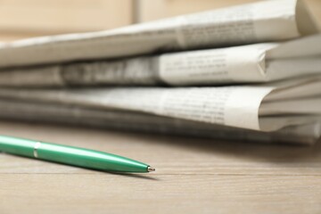 Stack of newspapers and pen on wooden table, closeup