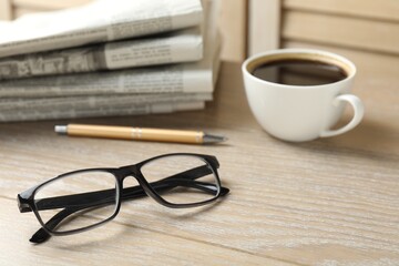 Stack of newspapers, coffee, pen and glasses on wooden table, closeup
