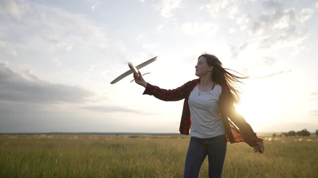 Launching toy airplane into sky at sunset girl runs through grass field playing with foam plane hair blowing in wind against glowing horizon sky warm light capturing carefree play summer energy