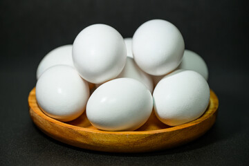 검정색 배경 앞 나무 그릇에 담긴 흰색 계란들 