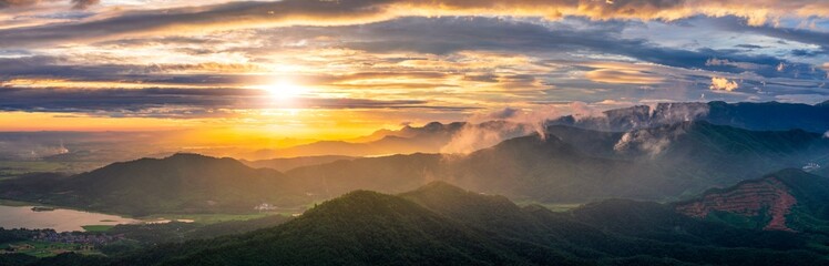 Breathtaking mountain landscape with fog and clouds settled in the green forest valleys during a beautiful and golden sunset.