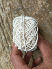 A white yarn ball held in a human hand with a natural background, showing fiber texture and soft details under warm natural light.