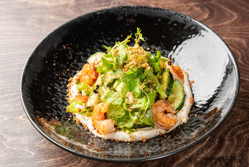 Gourmet salad with cucumbers, orange slices, greens, seeds, and creamy dressing on a dark ceramic plate. Rustic wooden background. Fresh, vibrant, and artfully plated.
