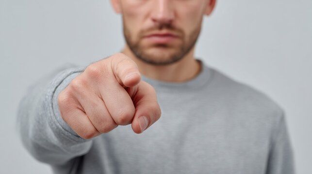 Confident man pointing finger at viewer against neutral gray background conveying assertiveness and direct engagement in a powerful posture