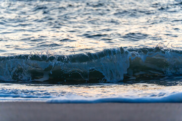 A breaking wave freezes mid-motion, revealing crystal details and sea foam. The evening light gives the water a soft blue tone.