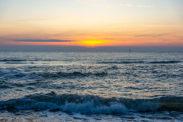 Soft evening colors glow above the calm sea at sunset. Gentle waves shimmer under orange and blue skies.