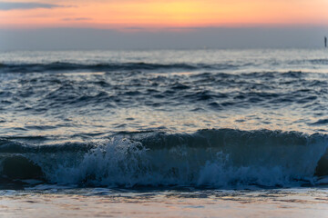 Small waves roll toward the shore beneath a pastel sunset sky. The soft colors reflect the evening calm of the sea.