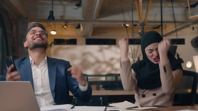 Happy Arabian business team winning with phone giving high five excited job two colleagues in office man with woman in hijab Muslim businessman with businesswoman smartphone achive victory success