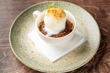 Vanilla ice cream melting over warm chocolate cake in a white cup, garnished with mint and crumbs, served on a green plate with napkin. Cozy, indulgent dessert presentation.