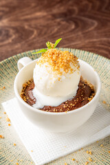 Vanilla ice cream melting over warm chocolate cake in a white cup, garnished with mint and crumbs, served on a green plate with napkin. Cozy, indulgent dessert presentation.
