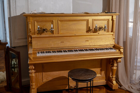 An antique piano, golden in color, in a vintage room.