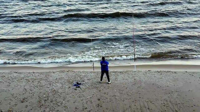 High-angle wide shot with a fixed camera showing one man fishing on the beach, standing at shore of rio de la plata river in Montevideo, Uruguay.