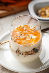 Healthy yogurt dessert served in a glass with granola, dried fruits and apricot jam, topped with almond flakes