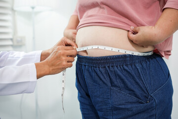 A doctor measures an Asian woman's waist during a routine health check-up to assess abdominal fat, obesity risk, and overall health status as part of preventive healthcare and weight management.