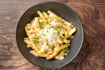 Golden French fries topped with creamy sauce, shredded cheese, and fresh herbs in a rustic bowl on wooden surface. Savory snack with rich texture and appetizing presentation.