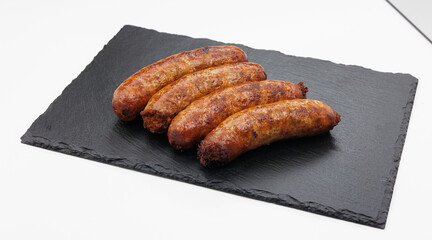 Four golden brown sausages arranged on a dark slate board offer a hearty, savory bite. Ideal for casual dining, barbecues, or menu photography in food and restaurant contexts.