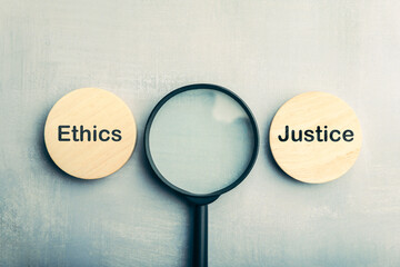 Magnifying glass between wooden blocks labeled ethics and justice, representing the idea of...