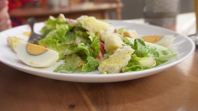 A woman eating Caesar Salad at restaurant. Served with crisp romaine lettuce, eggs, smoked beef, crunchy croutons, parmesan cheese, and a light Caesar dressing