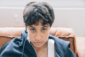Teenager looking seriously at viewer, resting indoors on a brown leather couch