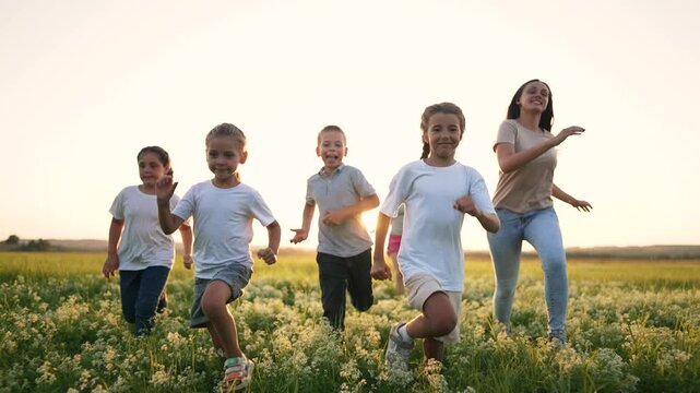 Run child and kid across field at sunset smile happy with friend on green grass under warm sun while group of children run toward foreground in open meadow laugh and play in breeze with warm sunlight