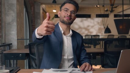 Arabian business man with laptop and documents showing thumb up in office Indian businessman guy writing notes analyze data male satisfied with like gesture approve financial growth success working  - Powered by Adobe
