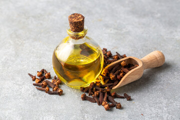 Close up glass bottle of essential clove oil and cloves in wooden spoon on rustic background. Herbs...