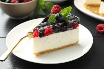 Piece of delicious cheesecake with berries and mint on black wooden table, closeup