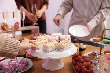 People taking different desserts from buffet table, closeup
