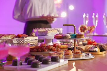 Different delicious desserts, drinks on buffet table and waiter, selective focus