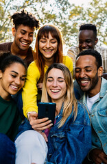 Vertical photo of young happy friends having fun together using mobile phone sitting outdoors....